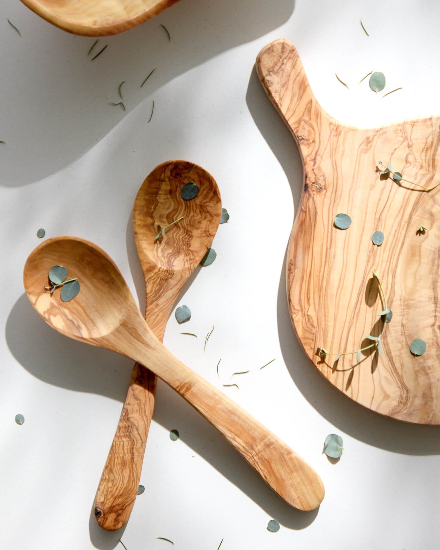
                  
                    Olive wood spoons and bread board with shadows cast and loose florals.
                  
                