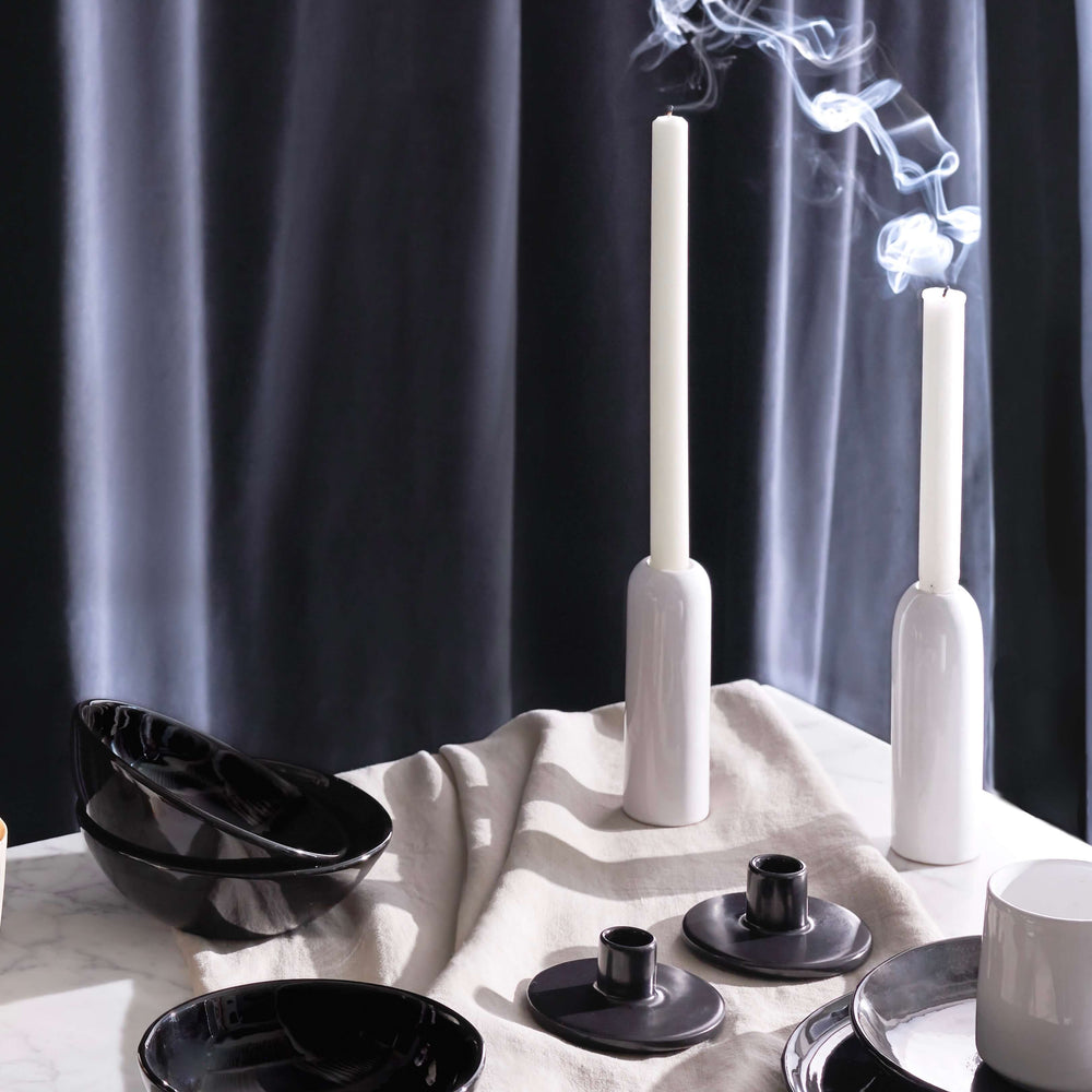 Luxury holiday table decor including glossy white ceramic taper holders with white candles and billowing smoke.