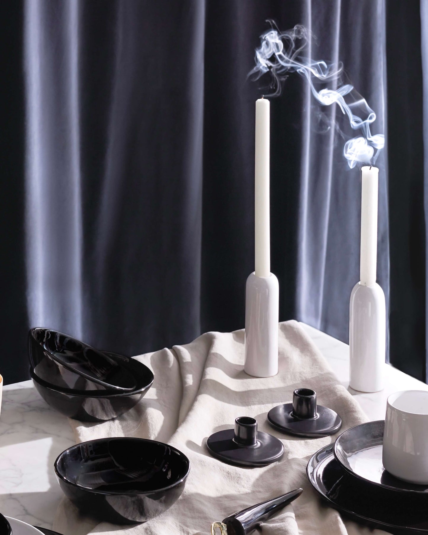 Luxury holiday table decor including glossy white ceramic taper holders with white candles and billowing smoke.