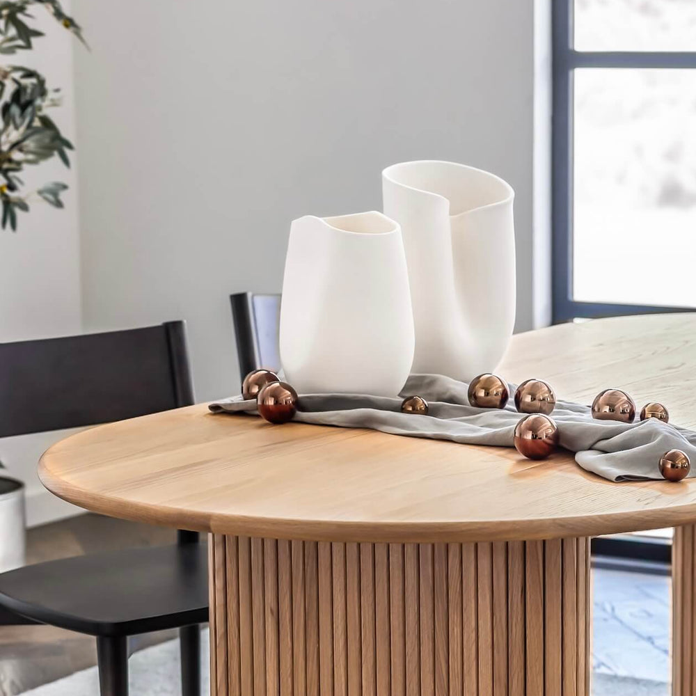 
                  
                    White sculptural terracotta vases as centerpiece on modern dining table with holiday ornaments.
                  
                