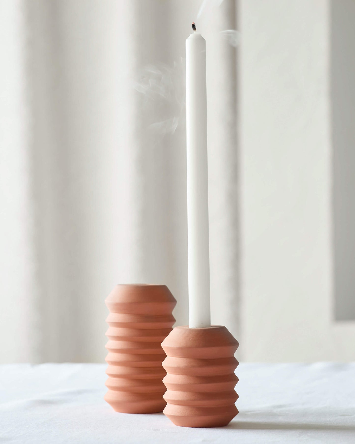 Kenza Terracotta taper holders by Fairkind on white table with modern white candle.