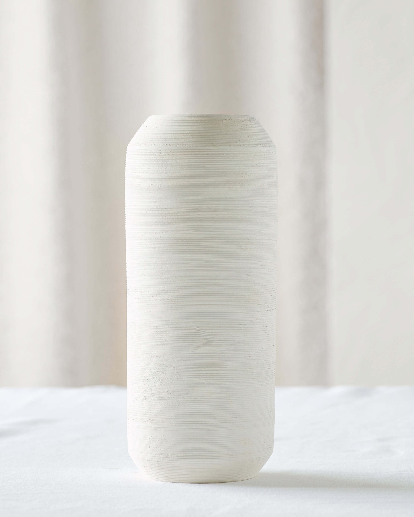 
                  
                    Medium Zarina Vase on white table. Tall oval vase with sculptural design and textured raw clay finish.
                  
                