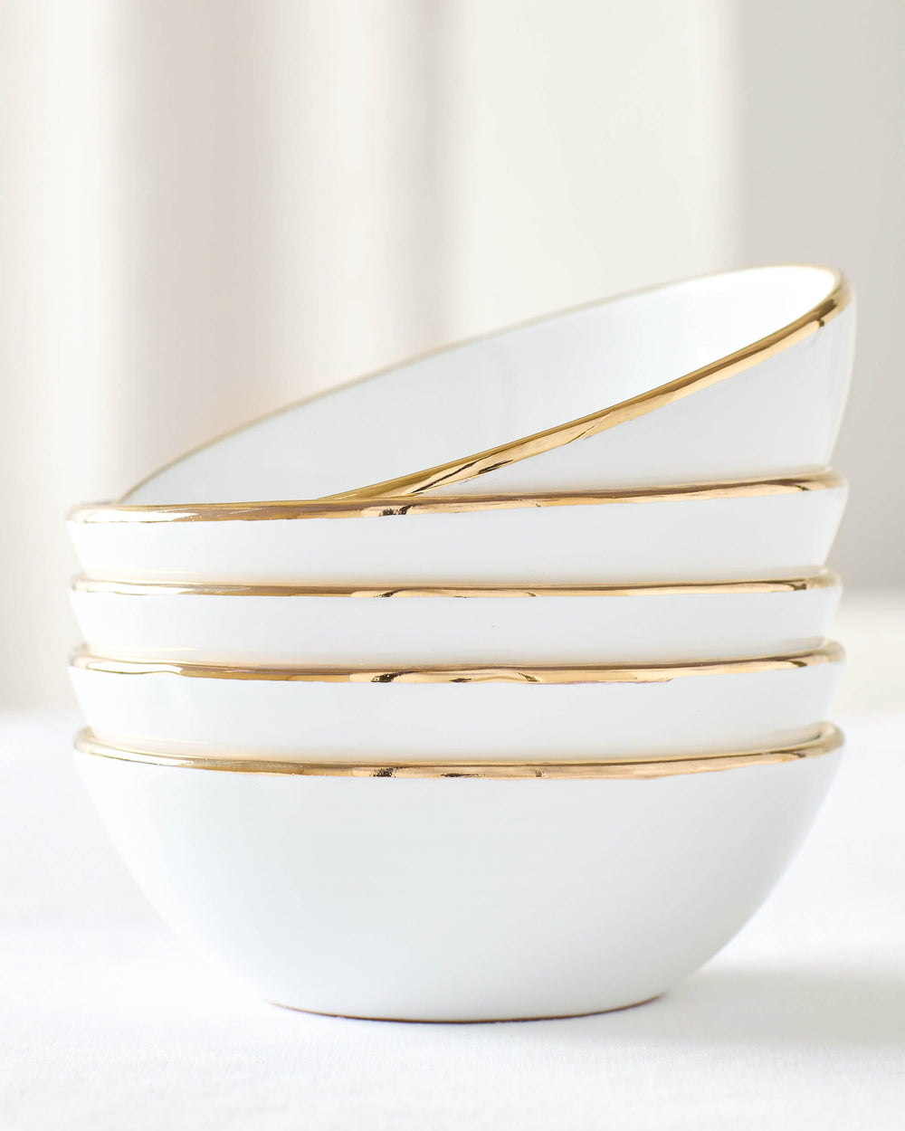 White ceramic soup bowls with 18k gold-rimmed edge stacked against white background. Fez Dinnerware by Fairkind.