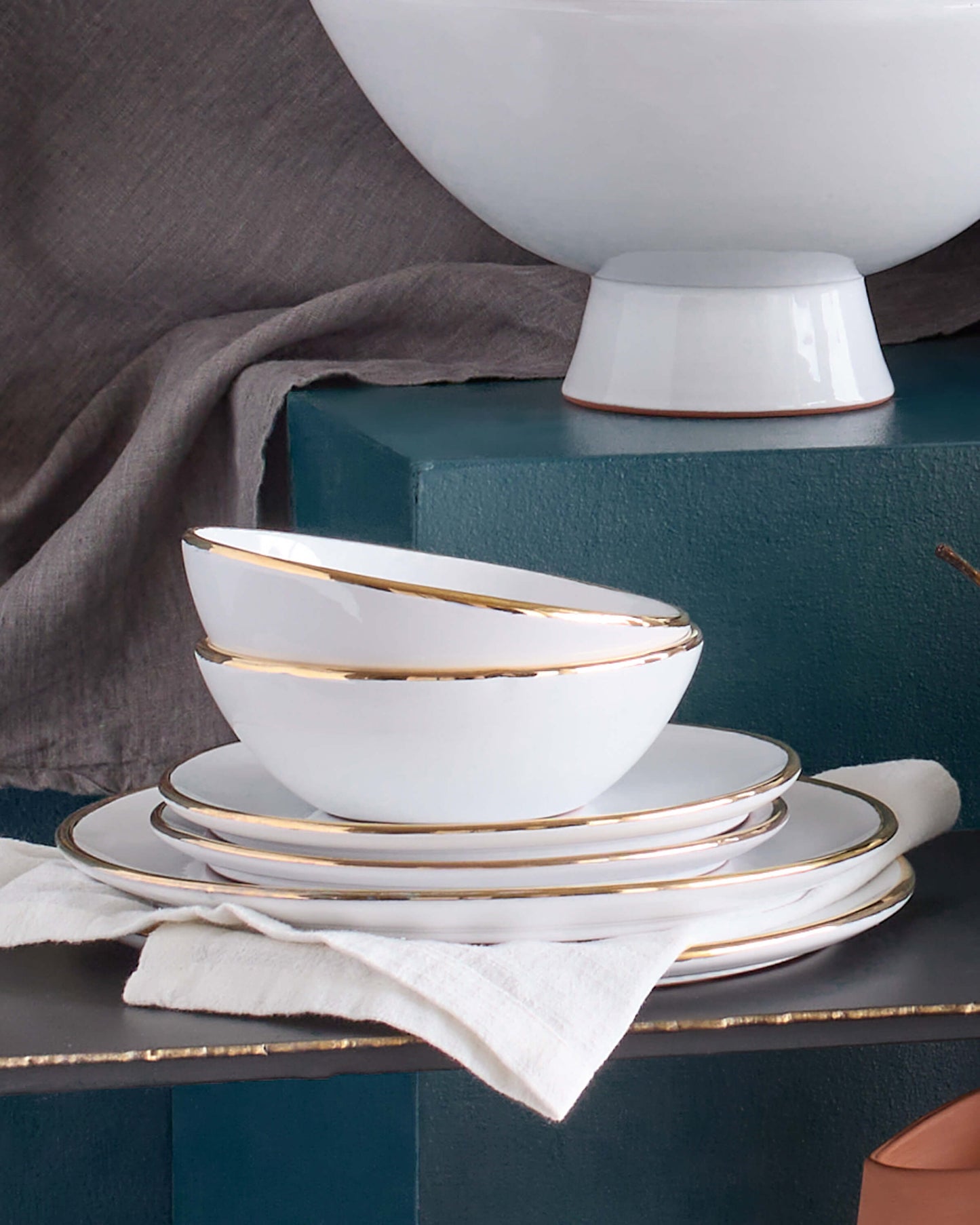 Handmade ceramic dinnerware with real gold edge stacked against blue background.