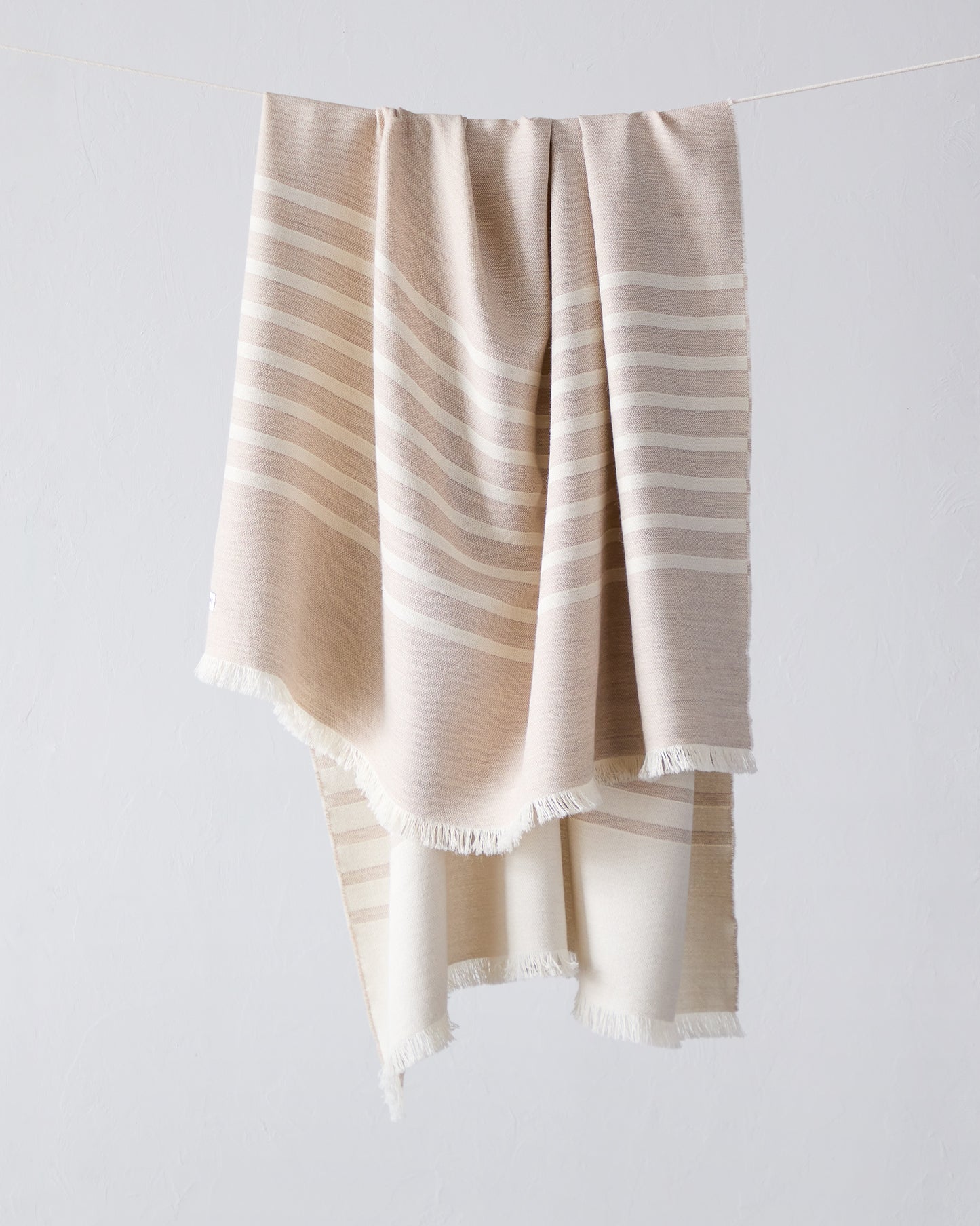 Fairkind Santiago sand alpaca throw blanket with baby alpaca soft tan base with modern white stripes and cream fringe.