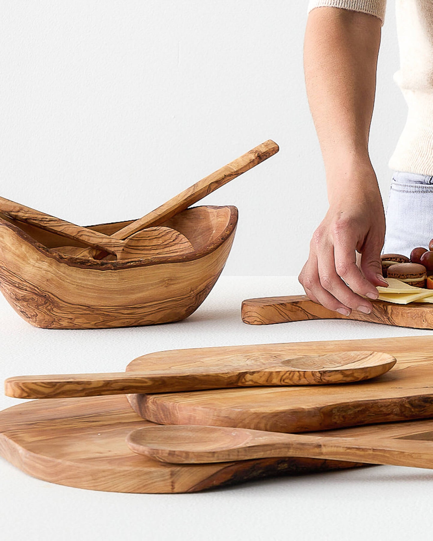 
                  
                    Woman creating cheeseboard in background with olive wood serving spoons in foreground.
                  
                