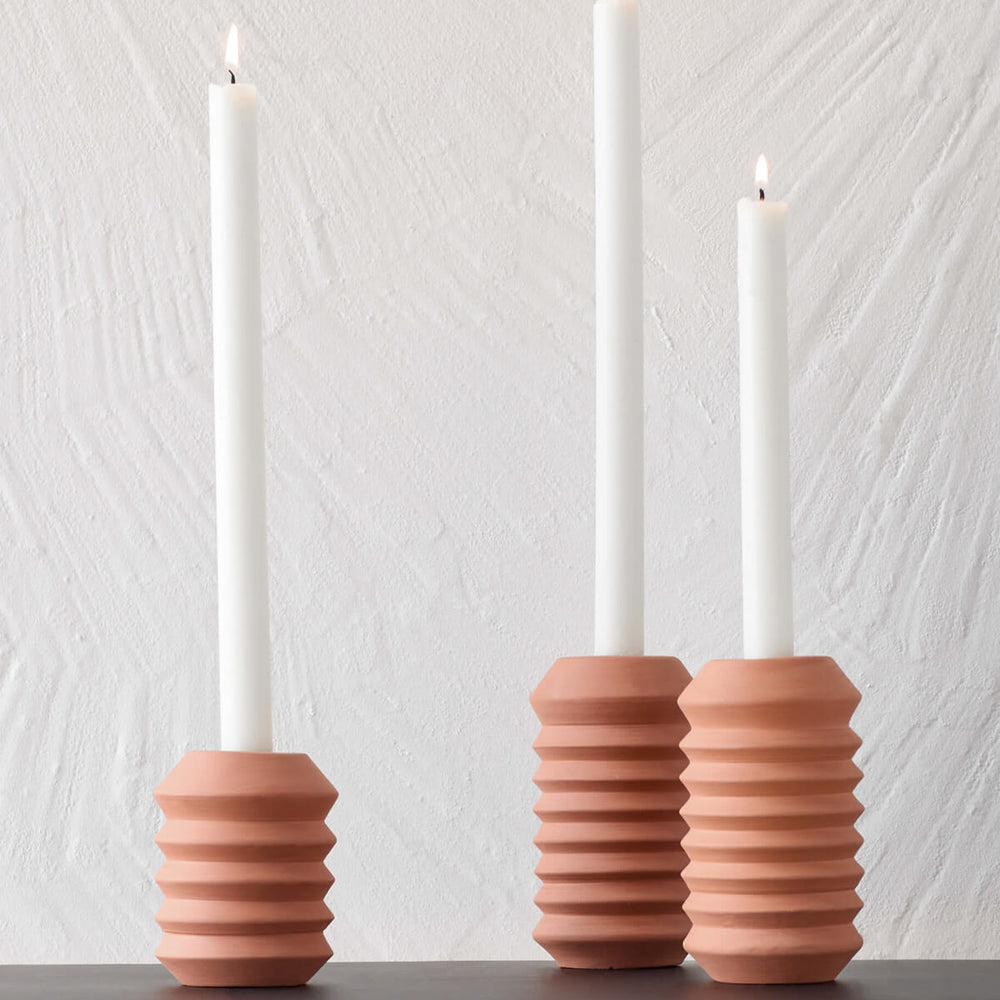 
                  
                    Modern, geometric Kenza Taper Holders by Fairkind styled with white taper candles on a sideboard.
                  
                
