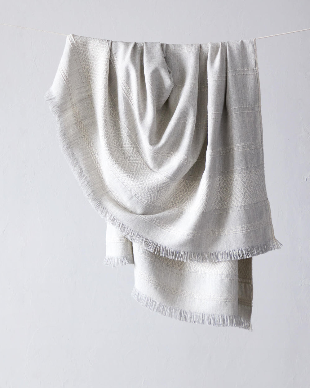 La Marea Alpaca Throw by Fairkind. Light gray textured baby alpaca throw blanket with fringe.