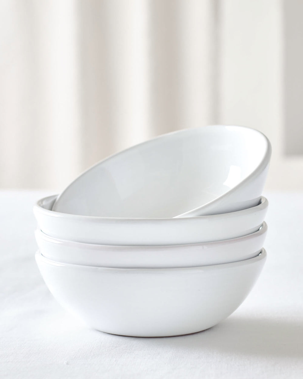Khira Soup Bowls by Fairkind stacked on white table. Modern, white ceramic dinnerware.