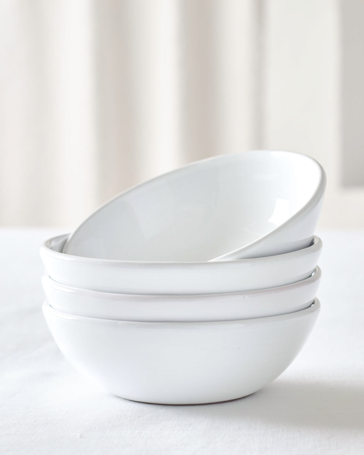 
                  
                    Khira Soup Bowls by Fairkind stacked on white table. Modern, white ceramic dinnerware.
                  
                