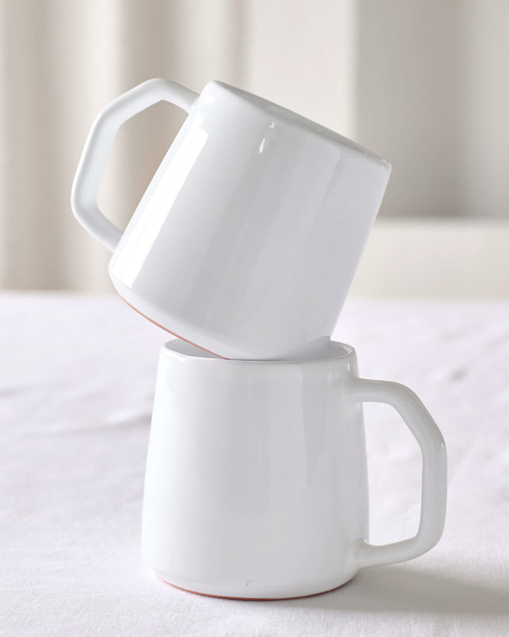 Khira white ceramic mug by Fairkind stacked on white table.