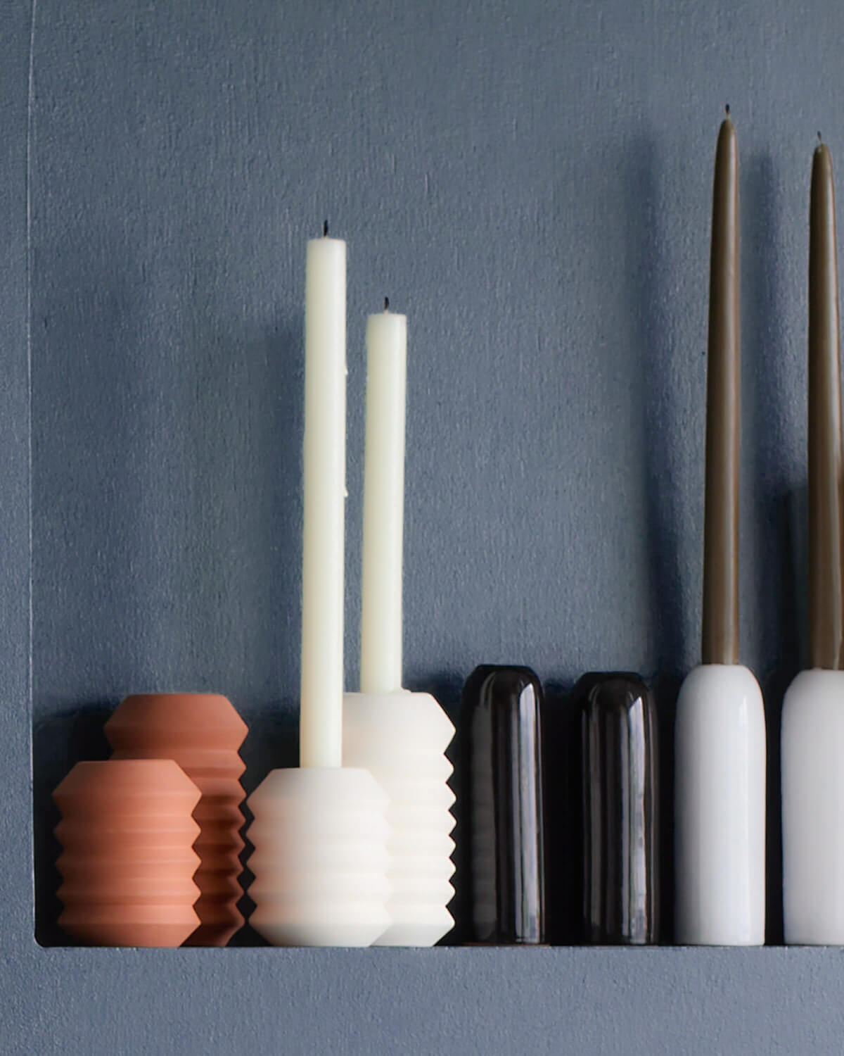 
                  
                    Taper candle holders from Fairkind's Morocco Collection lined up against blue wall.
                  
                