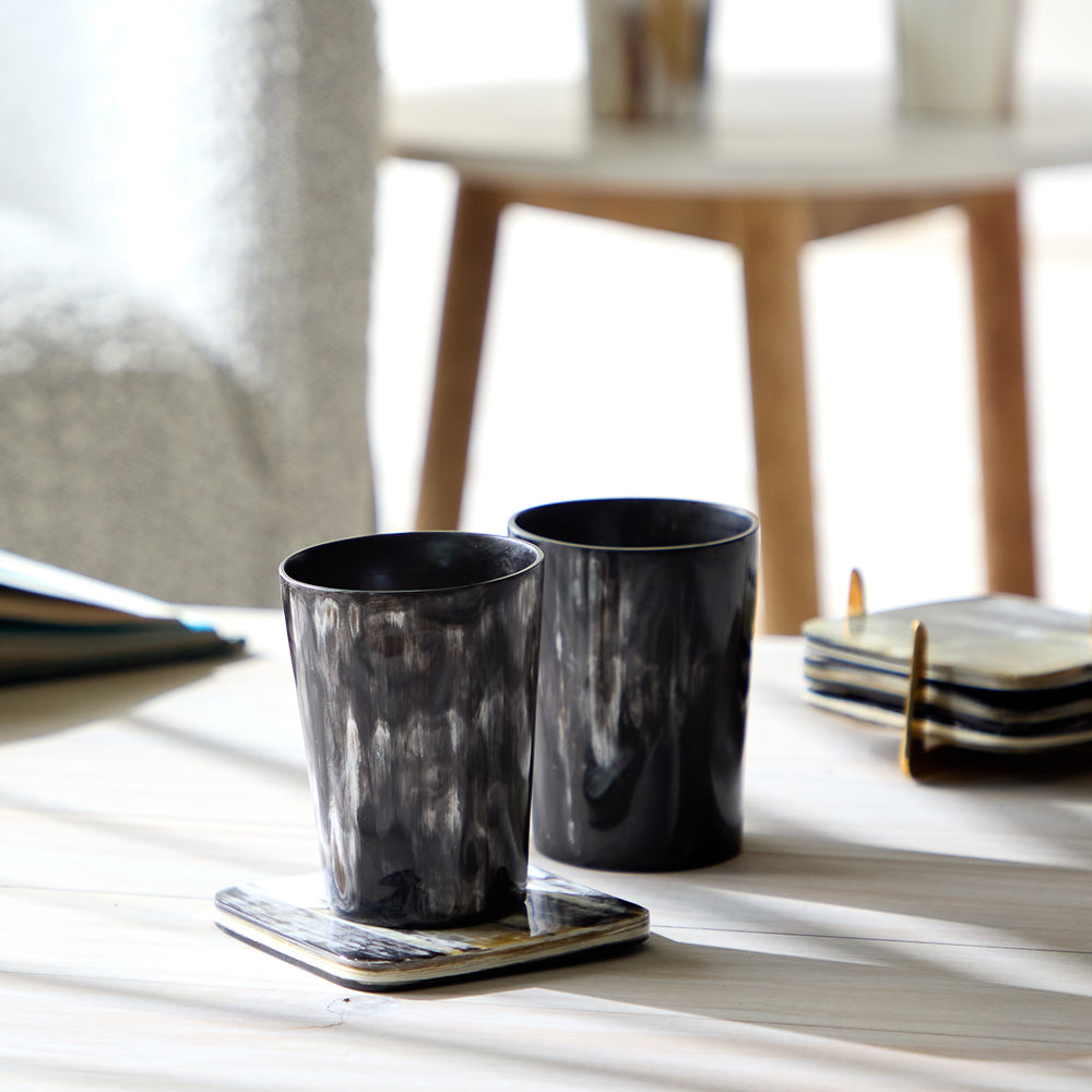 
                  
                    Bahati Tumbler set in dark horn on a coffee table with shadows cast.
                  
                