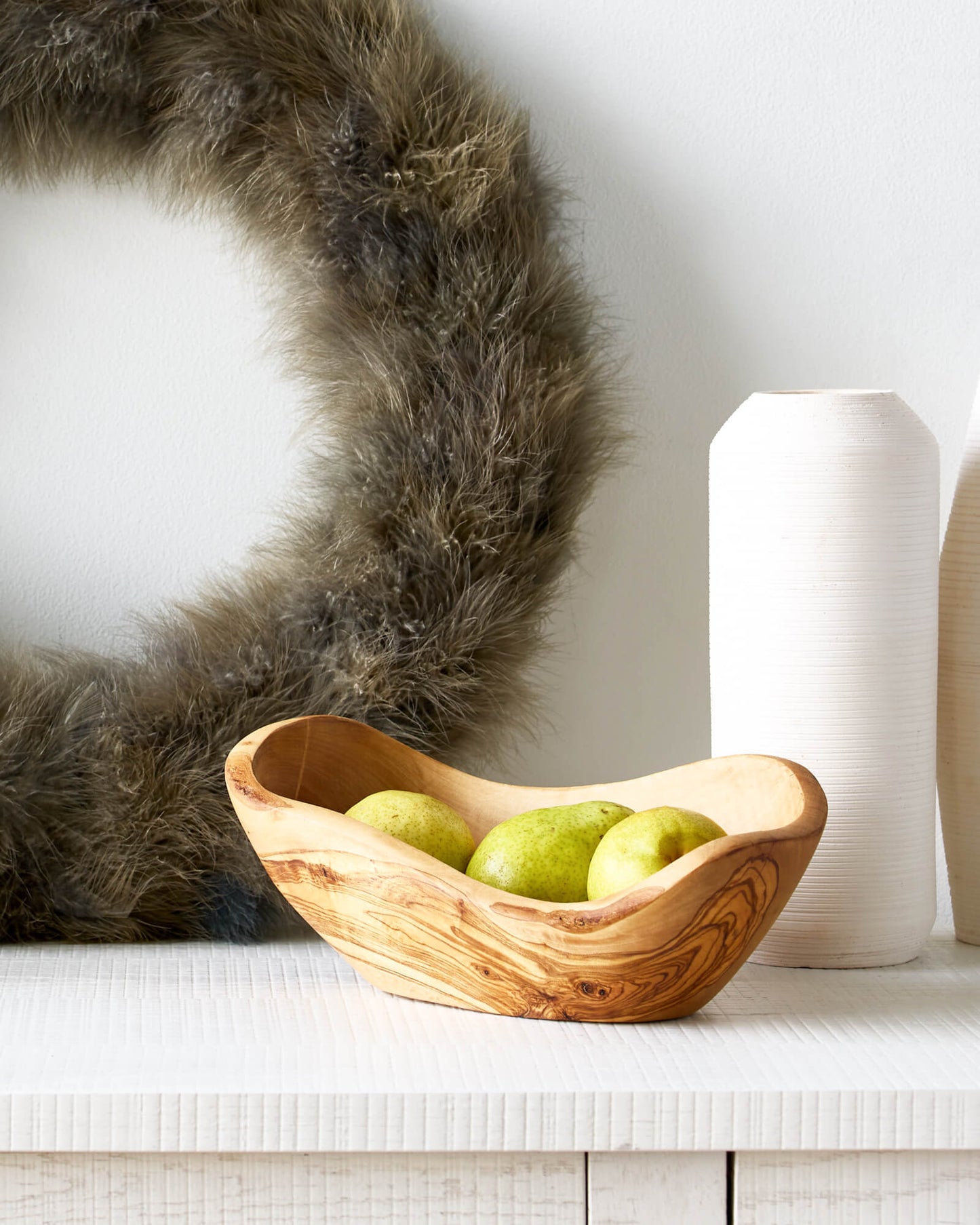 
                  
                    Holiday sideboard with wreath and olive wood serving bowl filled with fruit.
                  
                