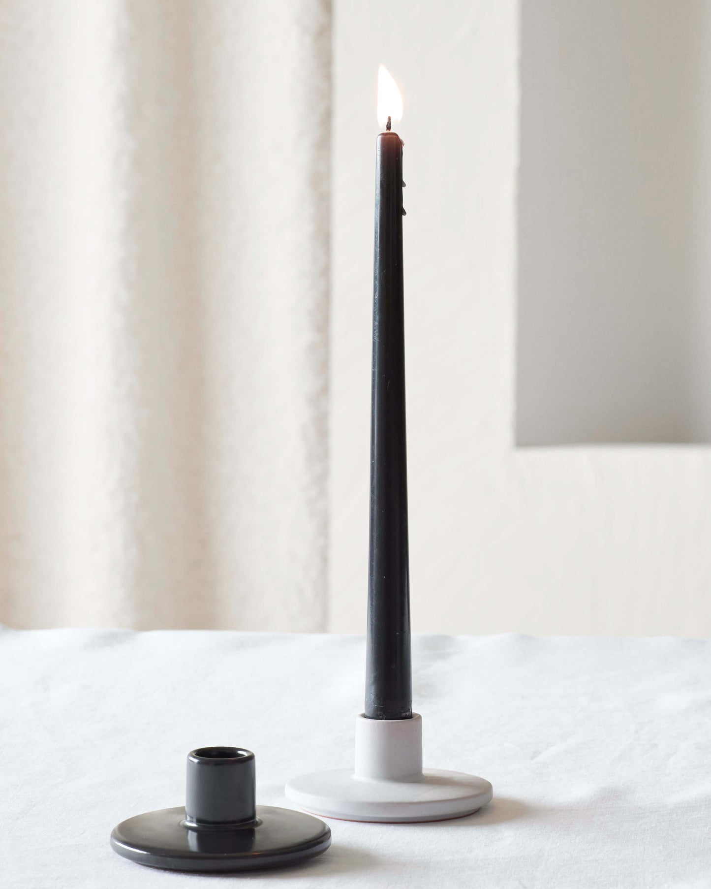 
                  
                    Safia ceramic taper holders by Fairkind in light gray and black on white table.
                  
                