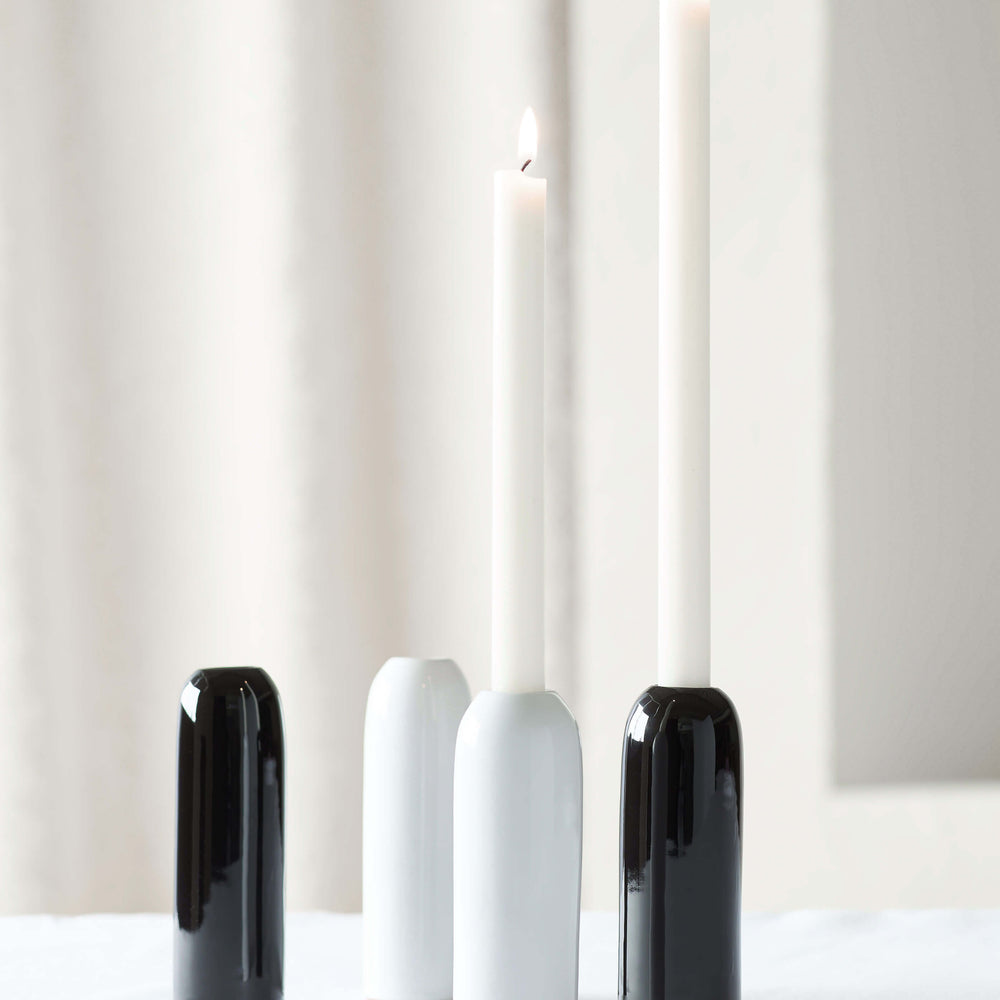 
                  
                    White and black Yasmine Taper Holders on white table with lit candles.
                  
                