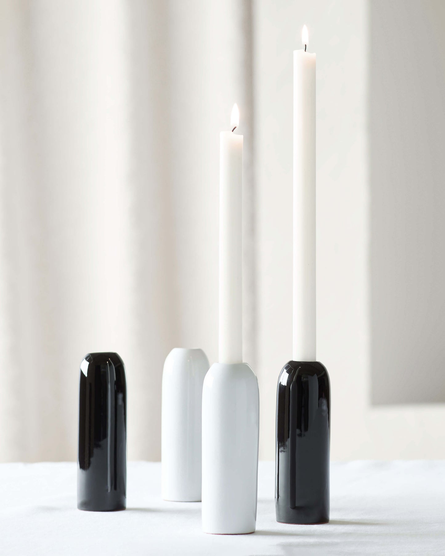 White and black Yasmine Taper Holders on white table with lit candles.