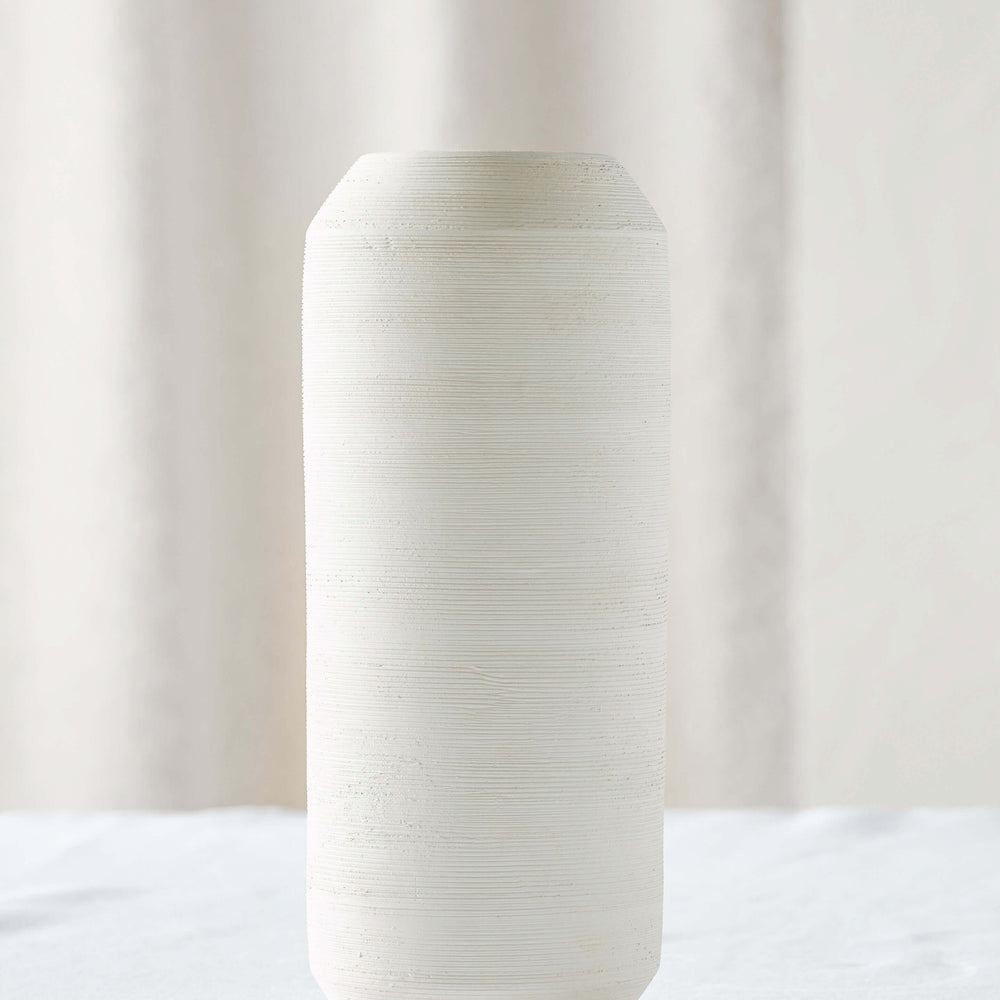 
                  
                    Medium Zarina Vase on white table. Tall oval vase with sculptural design and textured raw clay finish.
                  
                