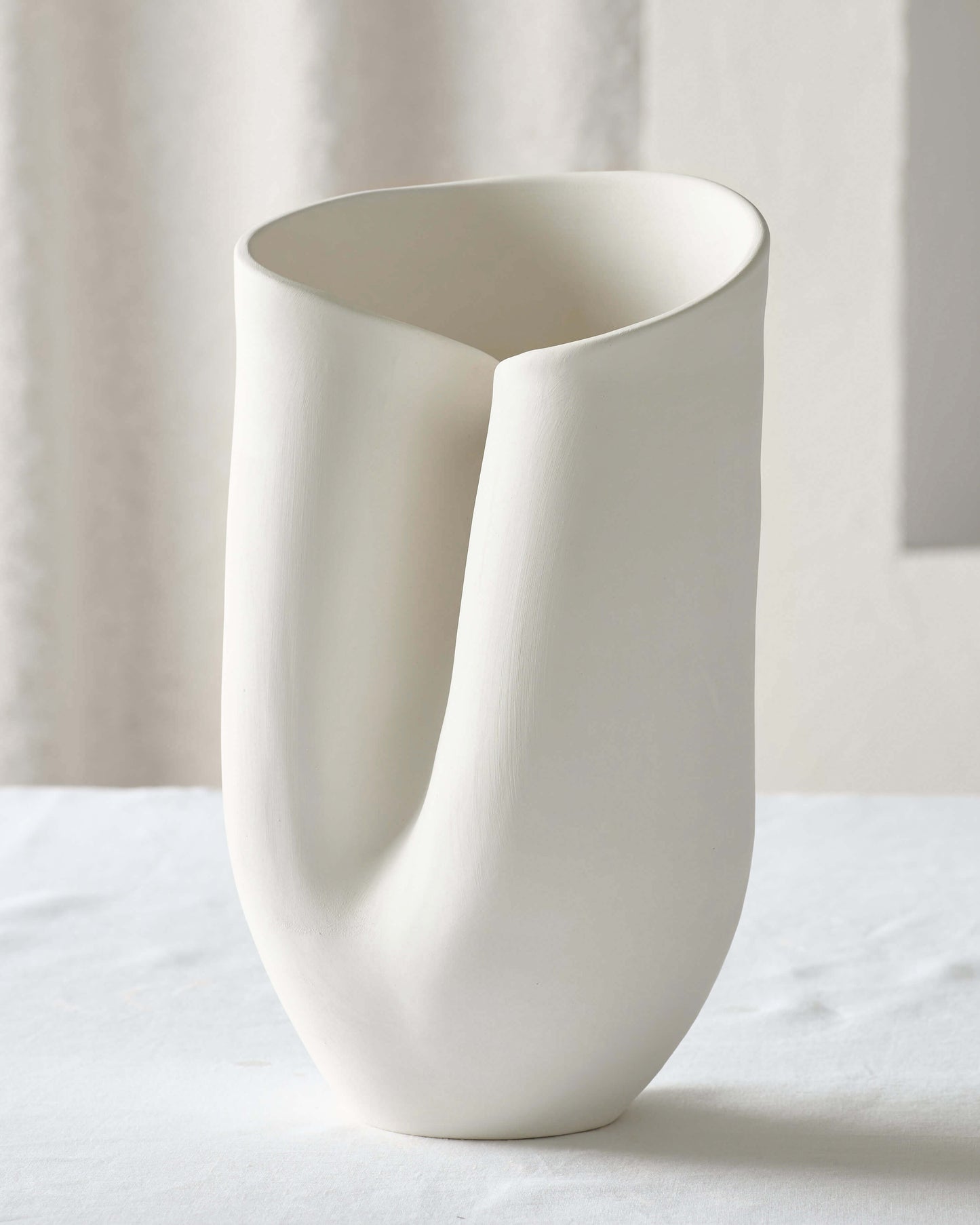 
                  
                    Large white Zoya Terracotta Vase on a white table. Abstract handcrafted vase with curved edge sculptural details and a textured finish.
                  
                