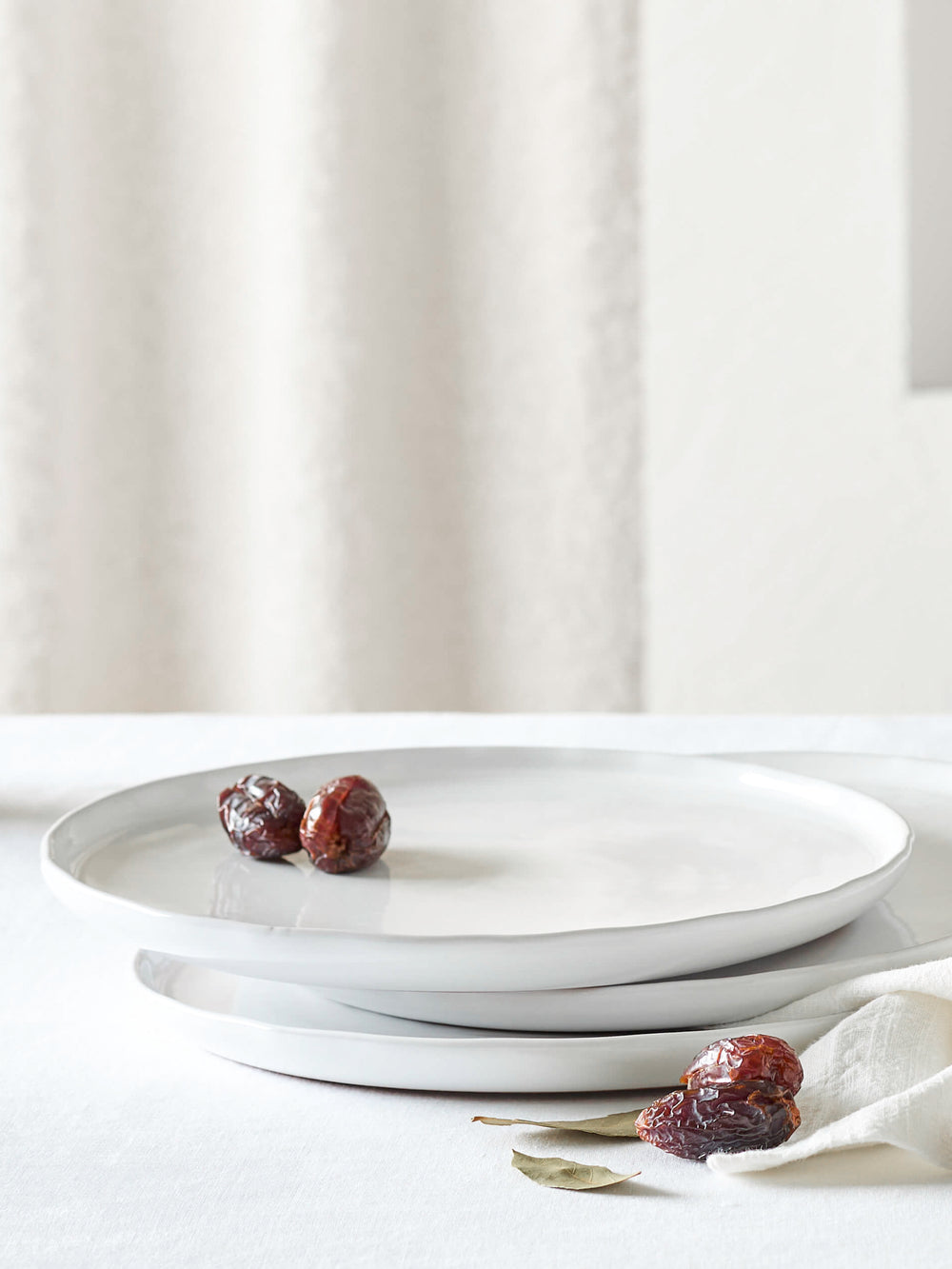 Fairkind's Khira Dinner Plates stacked on white table with fruit.