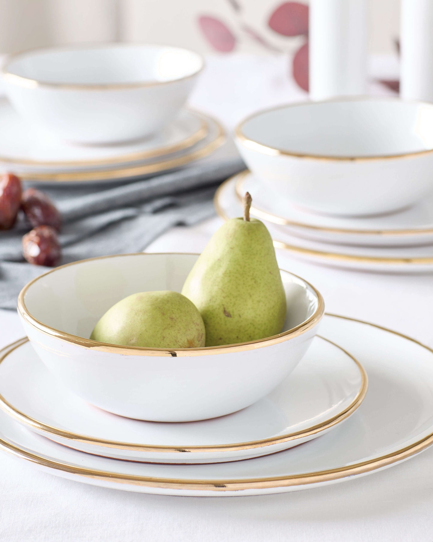 
                  
                    Fairkind's Fez Gold-Rimmed Dinnerware styled on a white table with pears.
                  
                