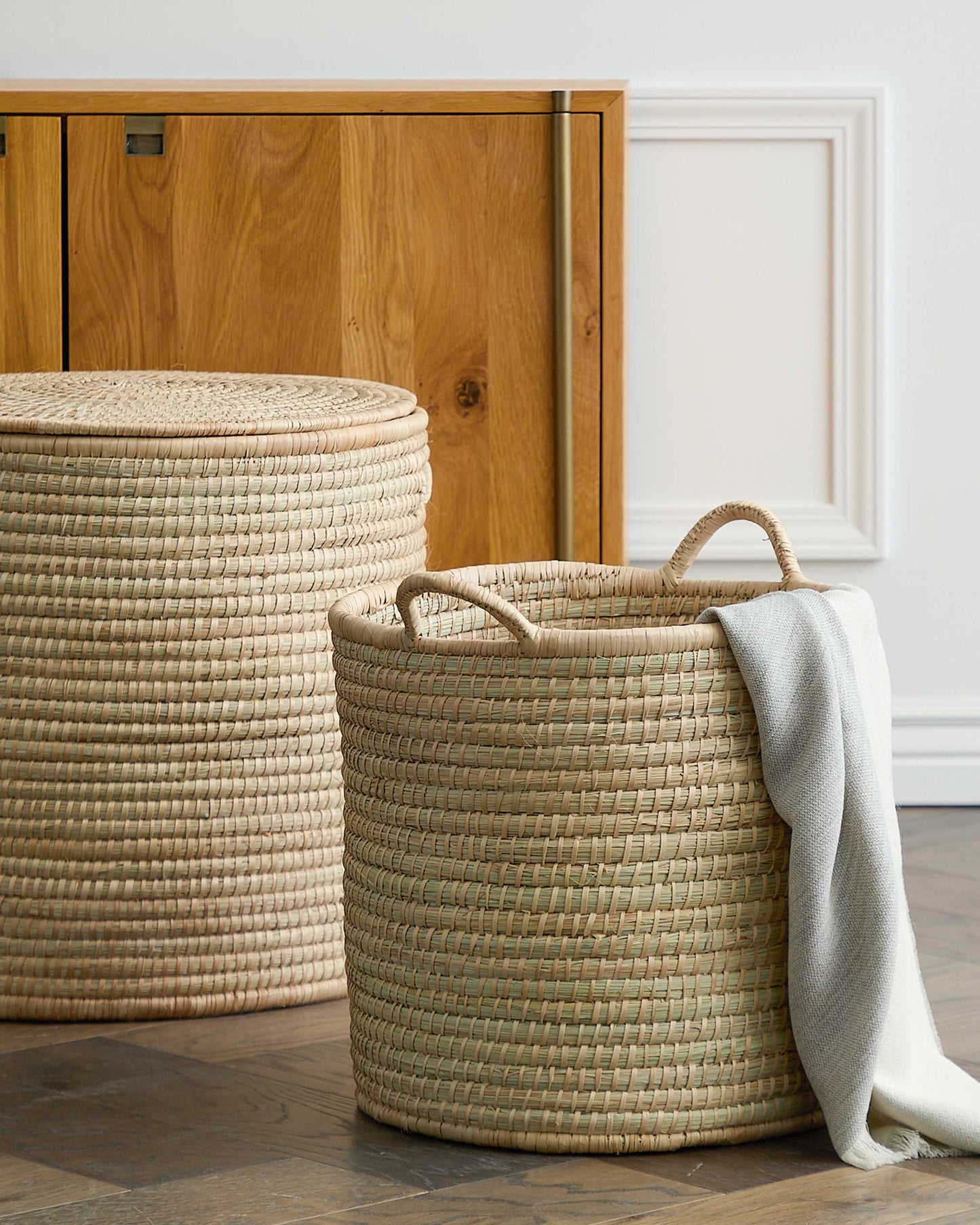 
                  
                    Woven storage basket with handles holding throw blanket in modern living room. 
                  
                