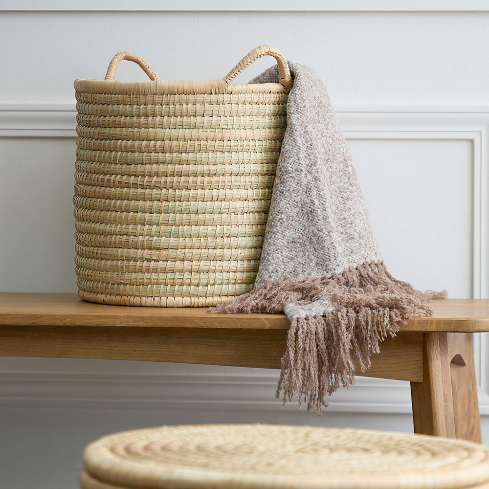 
                  
                    Small Luka Storage basket holding alpaca throw blanket on a bench in hallway. The Malawi Collection by Fairkind.
                  
                