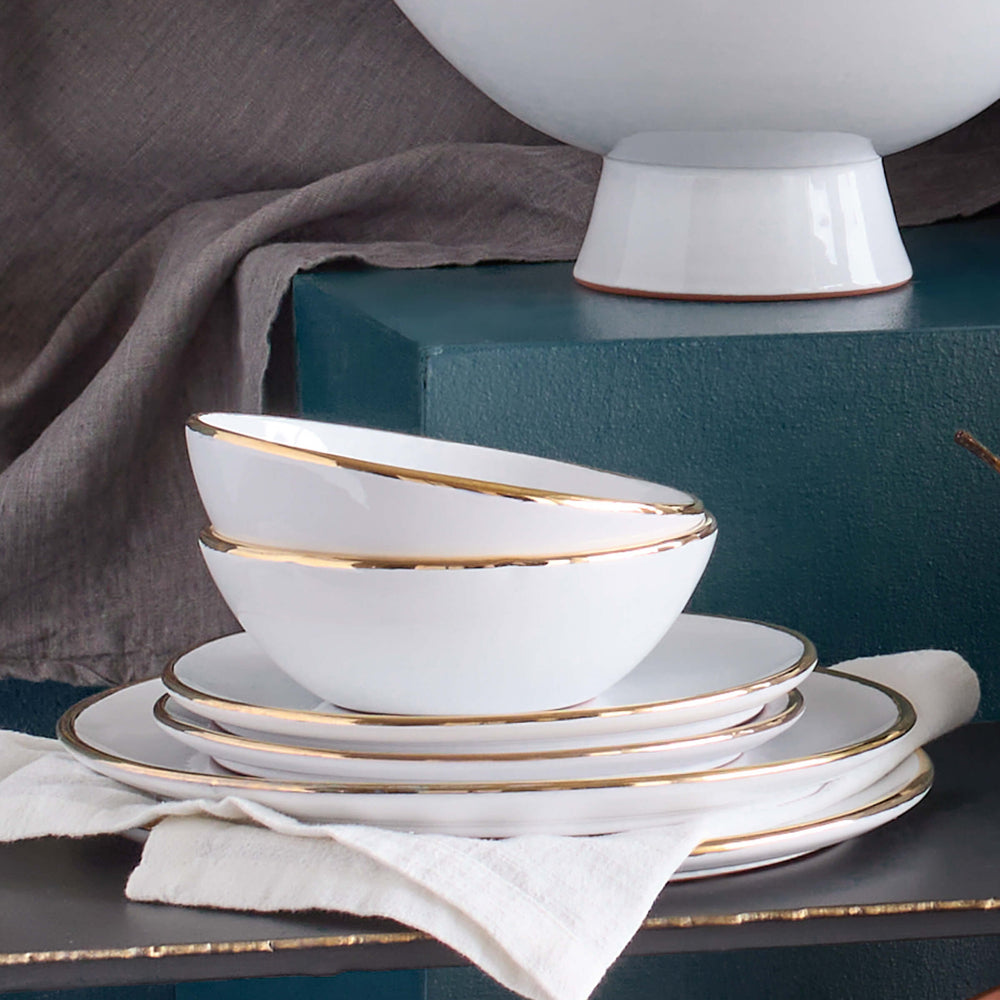 
                  
                    Handmade ceramic dinnerware with real gold edge stacked against blue background.
                  
                