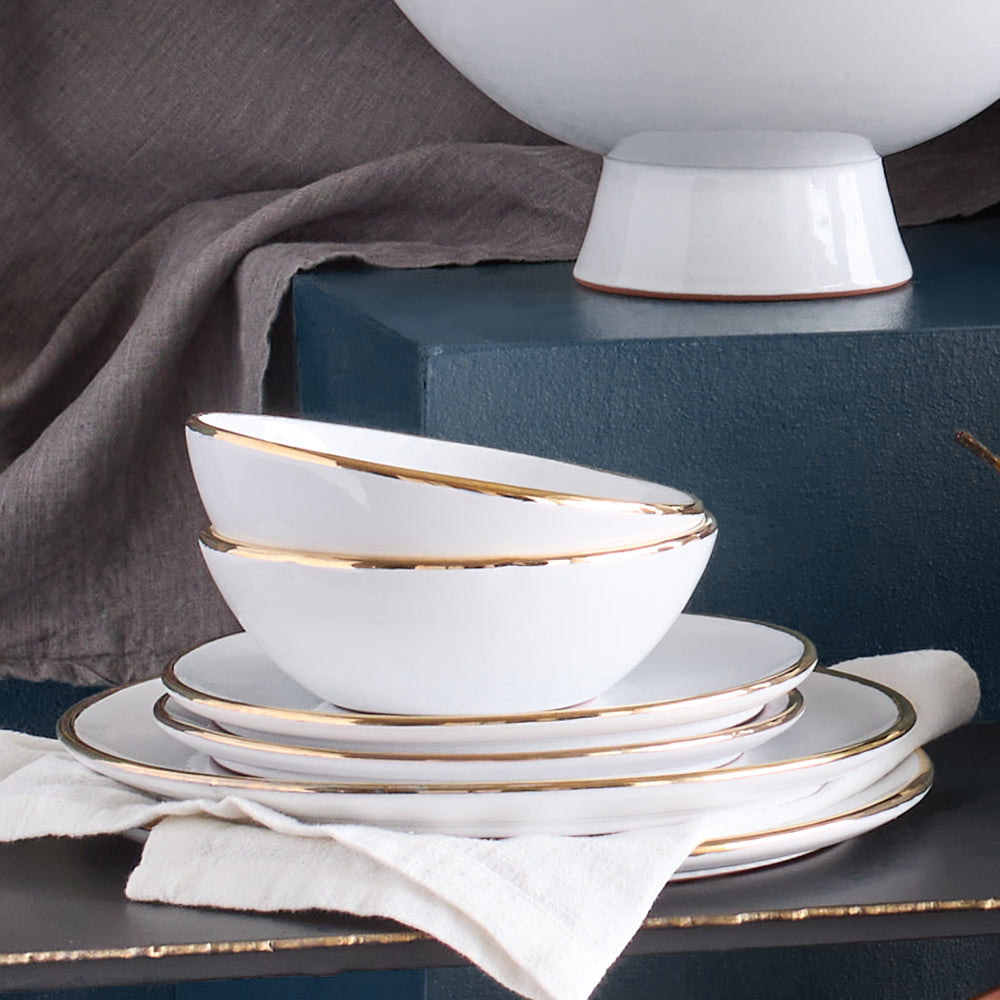 
                  
                    Gold-Rimmed Plates and Bowls stacked against blue wall. Fez Gold-Rimmed Dinnerware by Fairkind.
                  
                