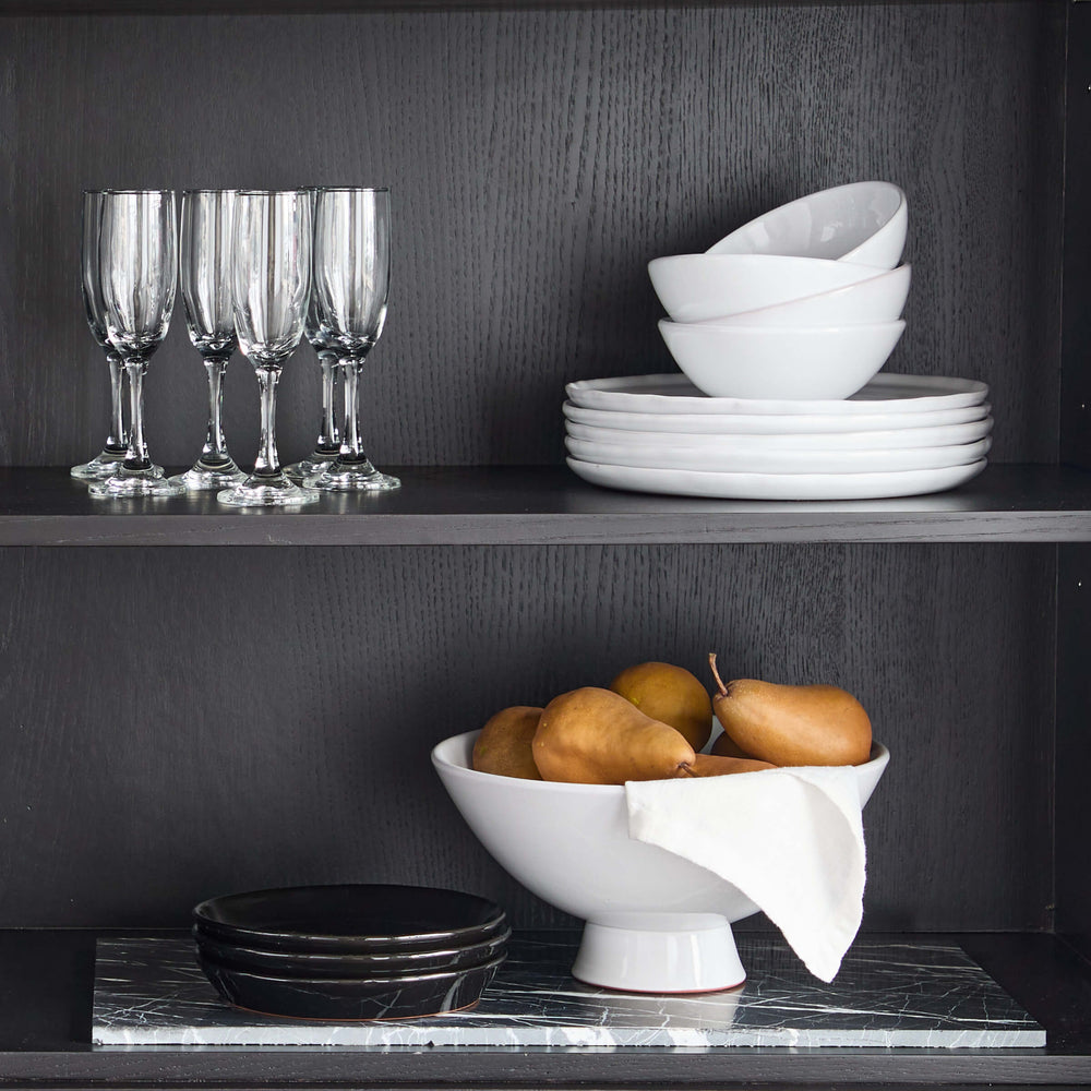 
                  
                    Modern hutch with ceramic dinnerware and white pedestal bowl filled with golden pears.
                  
                