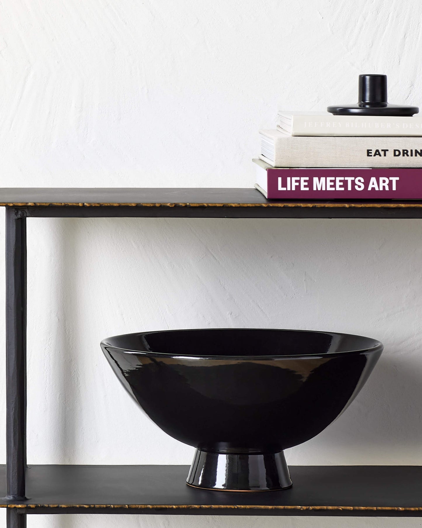 
                  
                    Bookshelf with black Safia Taper Holder stack on books and black Rami Pedestal Bowl on shelves.
                  
                