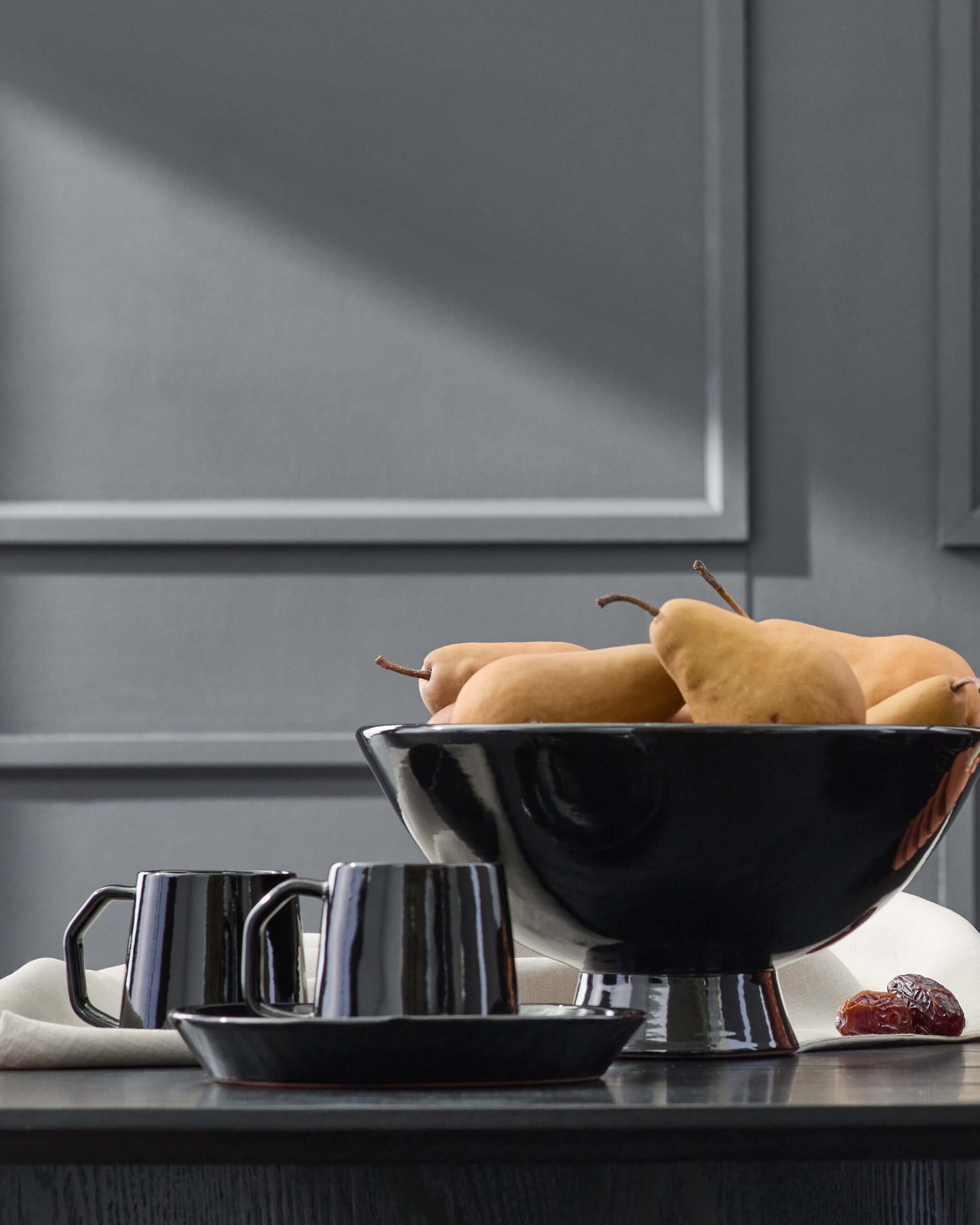 Black Riad Mugs styled on a dark wood table with fruit.