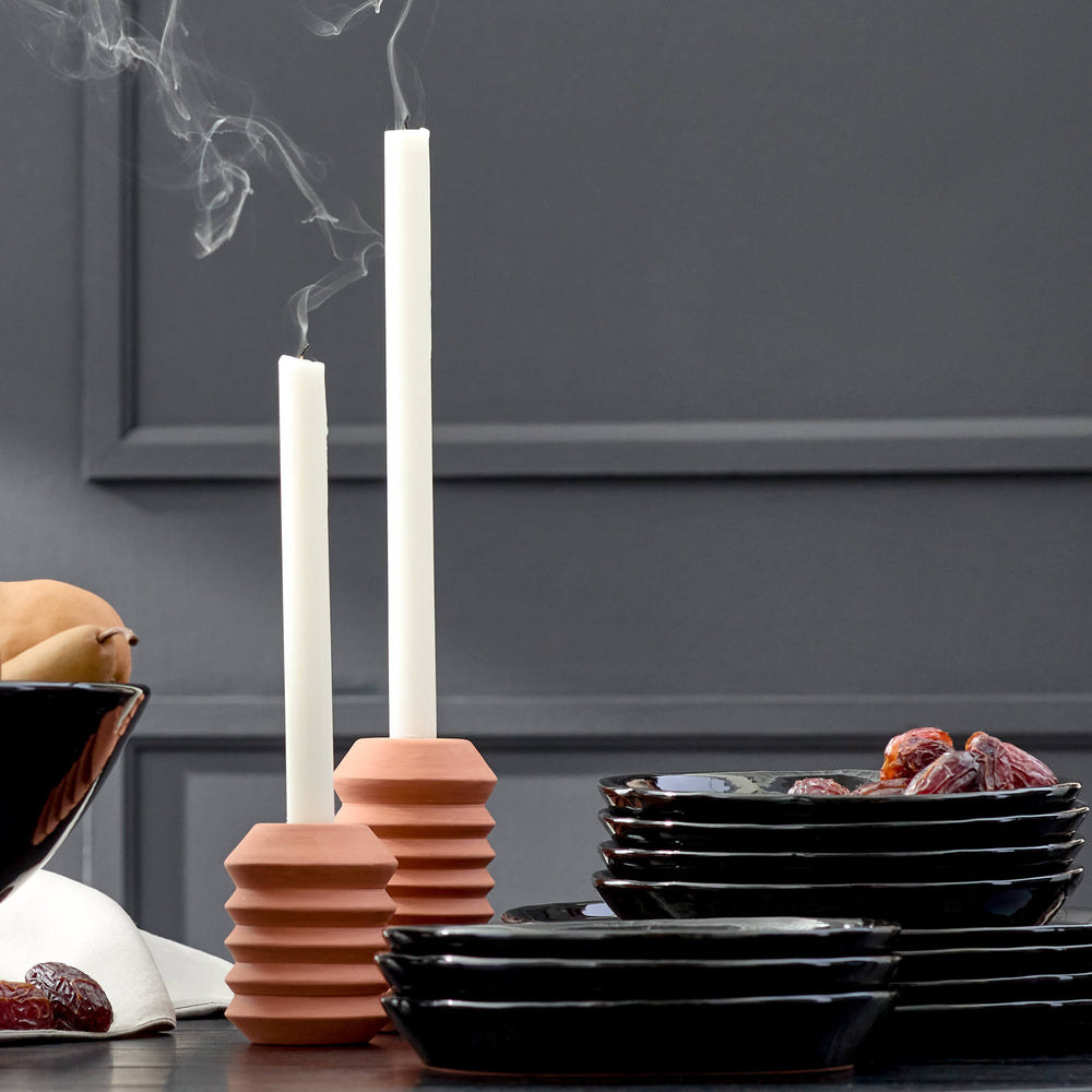 
                  
                    Black ceramic dinnerware styled on a tablescape with candles and fruit.
                  
                