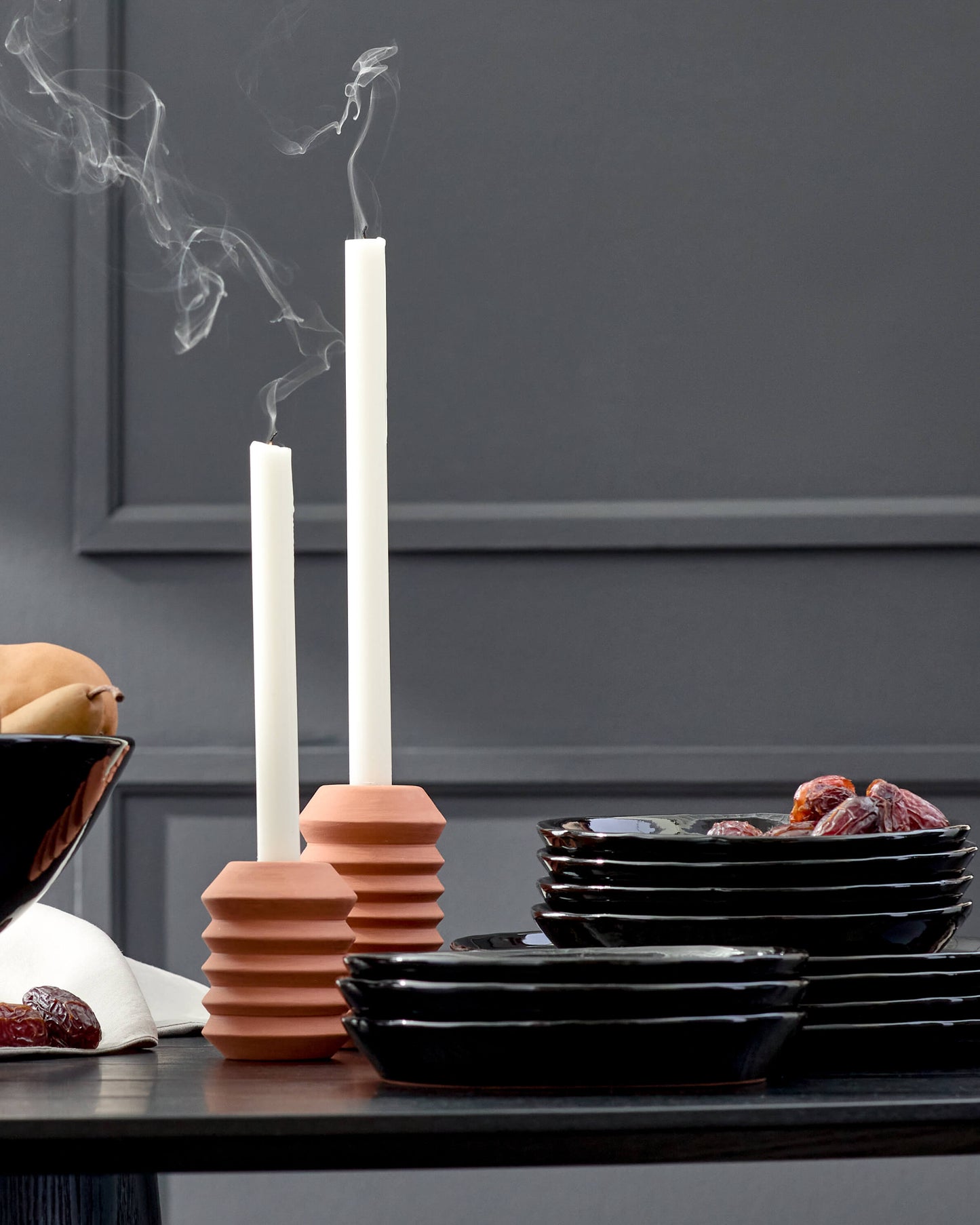 
                  
                    Black ceramic dinnerware styled on a tablescape with candles and fruit.
                  
                