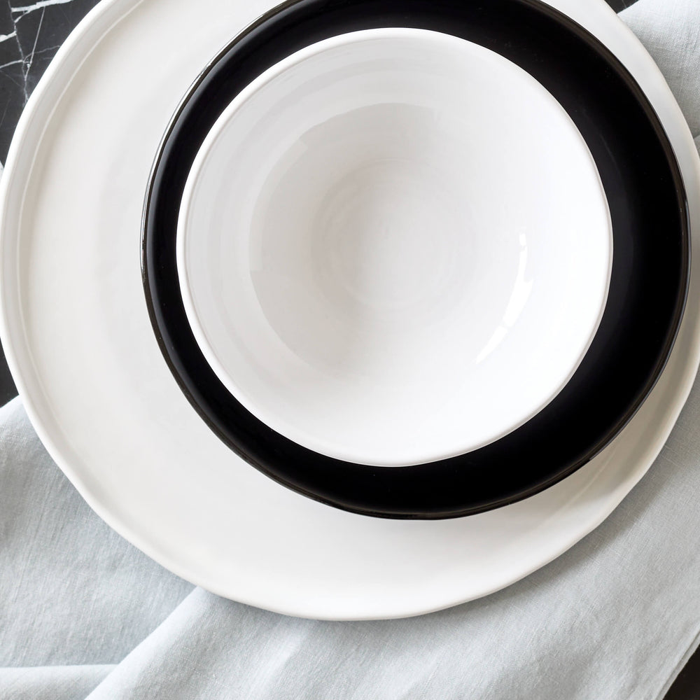 
                  
                    White Khira bowl stacked on black and white dinnerware set on a black marble table.
                  
                