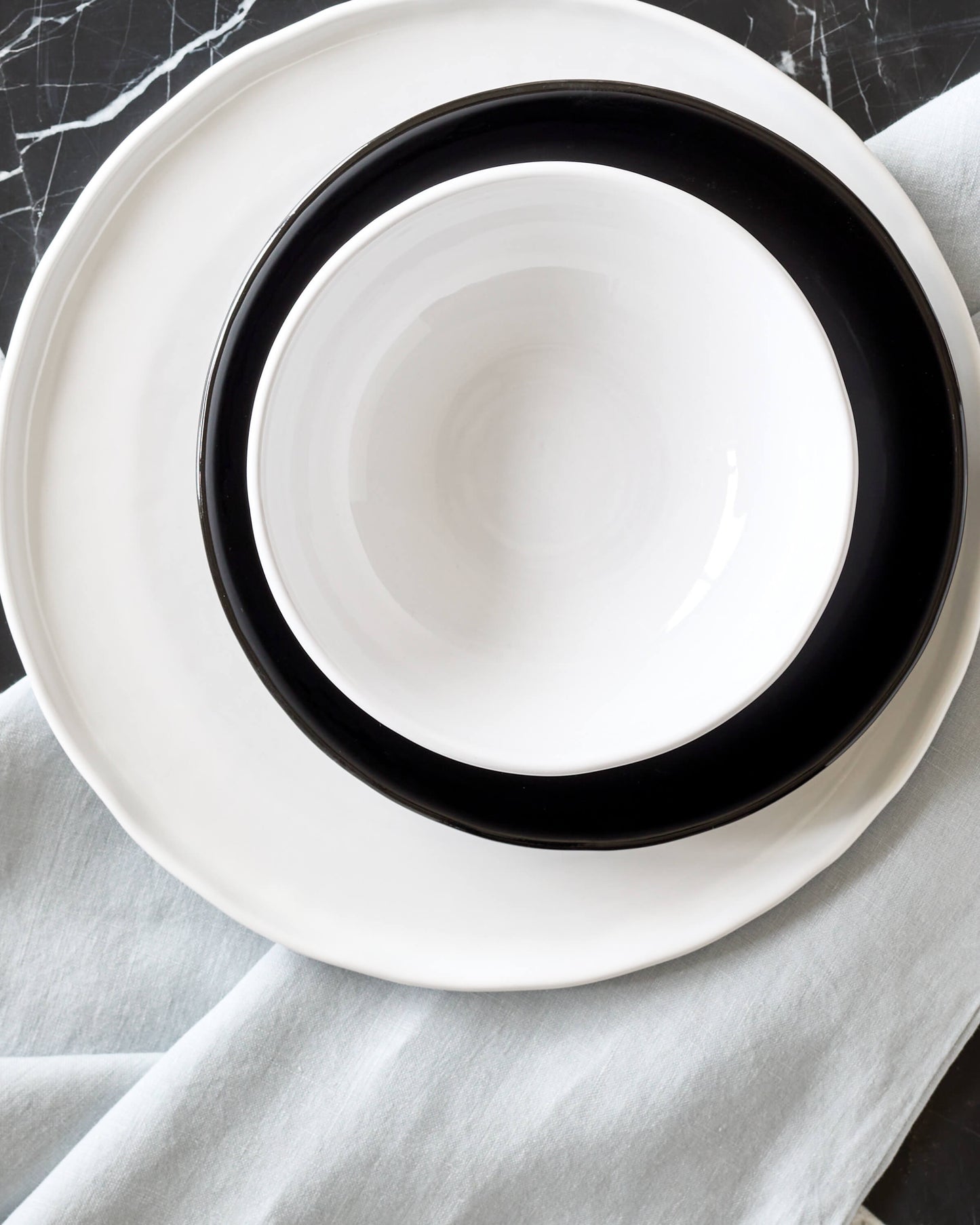 
                  
                    White Khira bowl stacked on black and white dinnerware set on a black marble table.
                  
                
