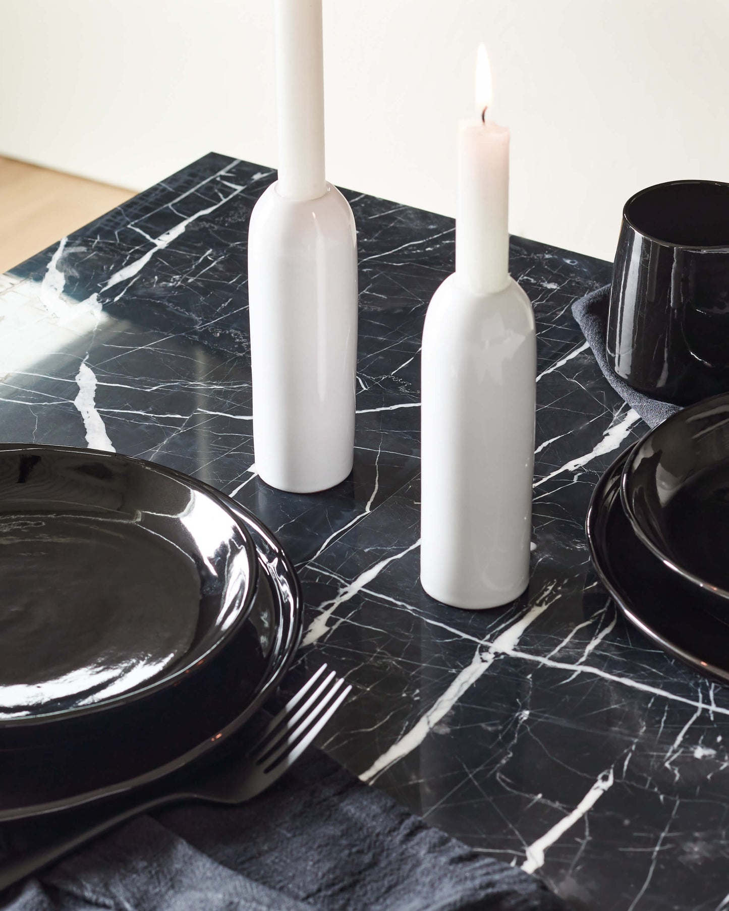 
                  
                    Yasmine Taper Holders in white styled with black dinnerware on a modern marble table. 
                  
                